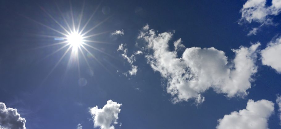 Bild på blå himmel med sol och vita moln.